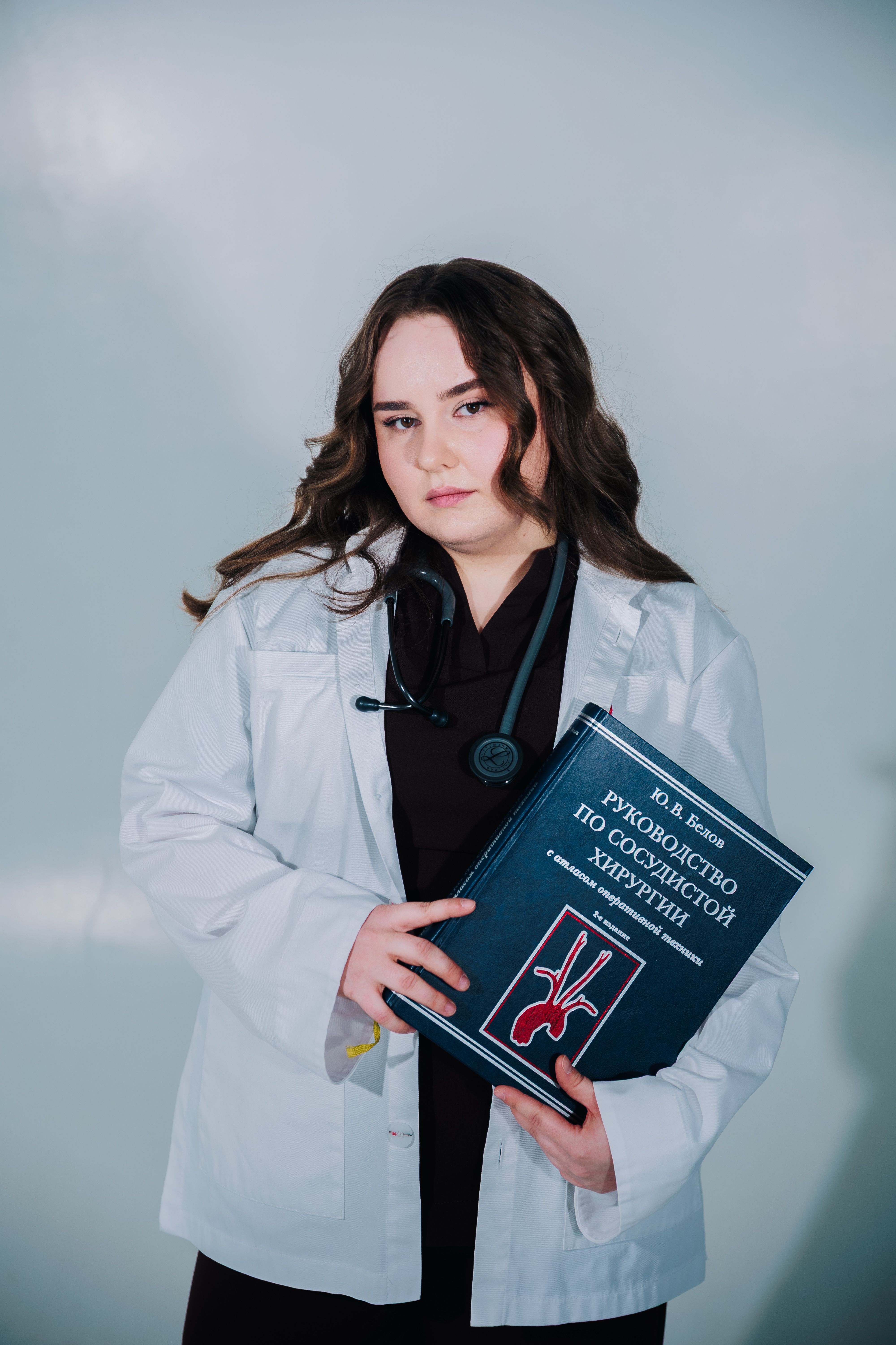 Young female doctor holding a surgical textbook against a neutral background.
