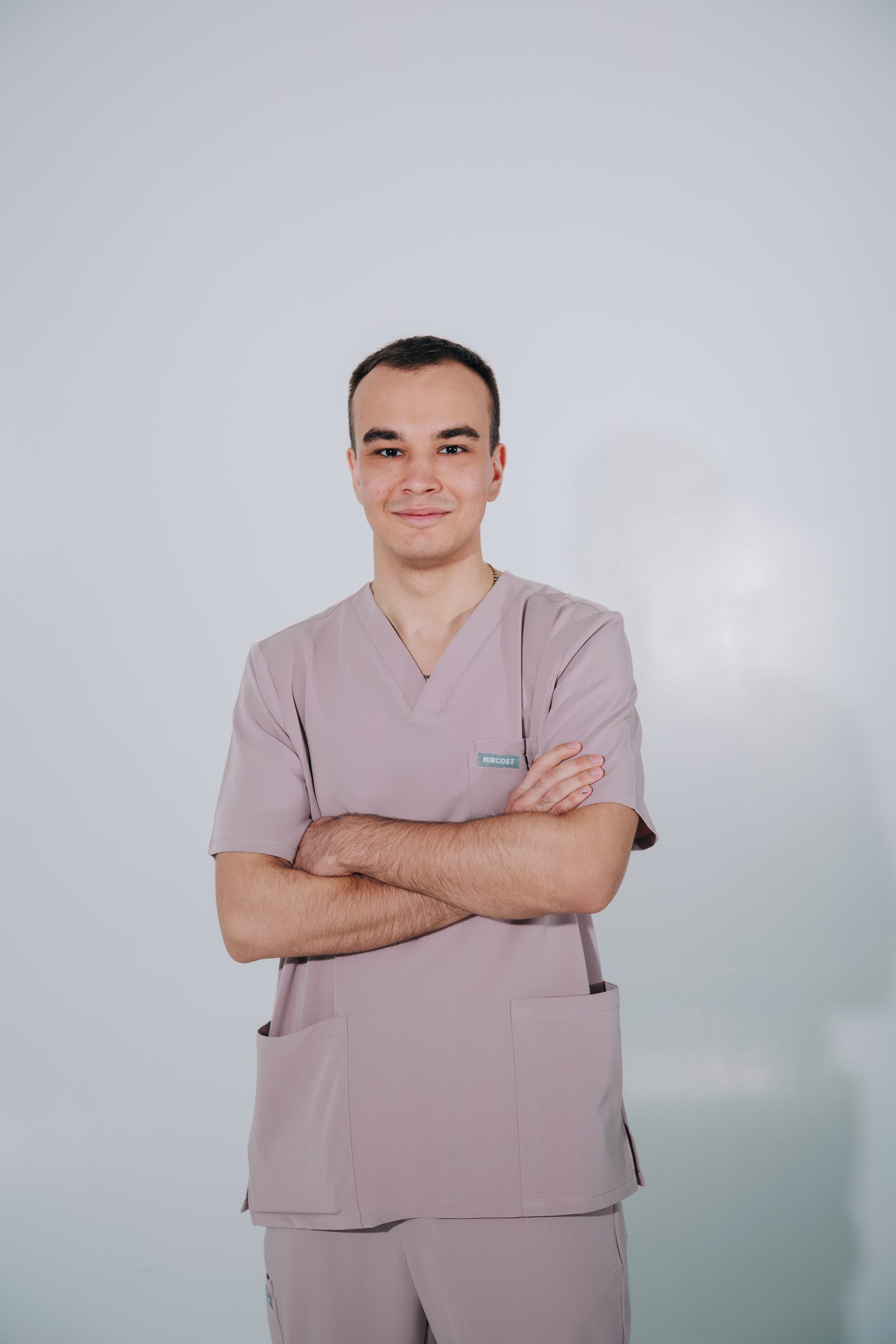 Portrait of a confident healthcare worker in pink medical scrubs indoors, arms crossed.