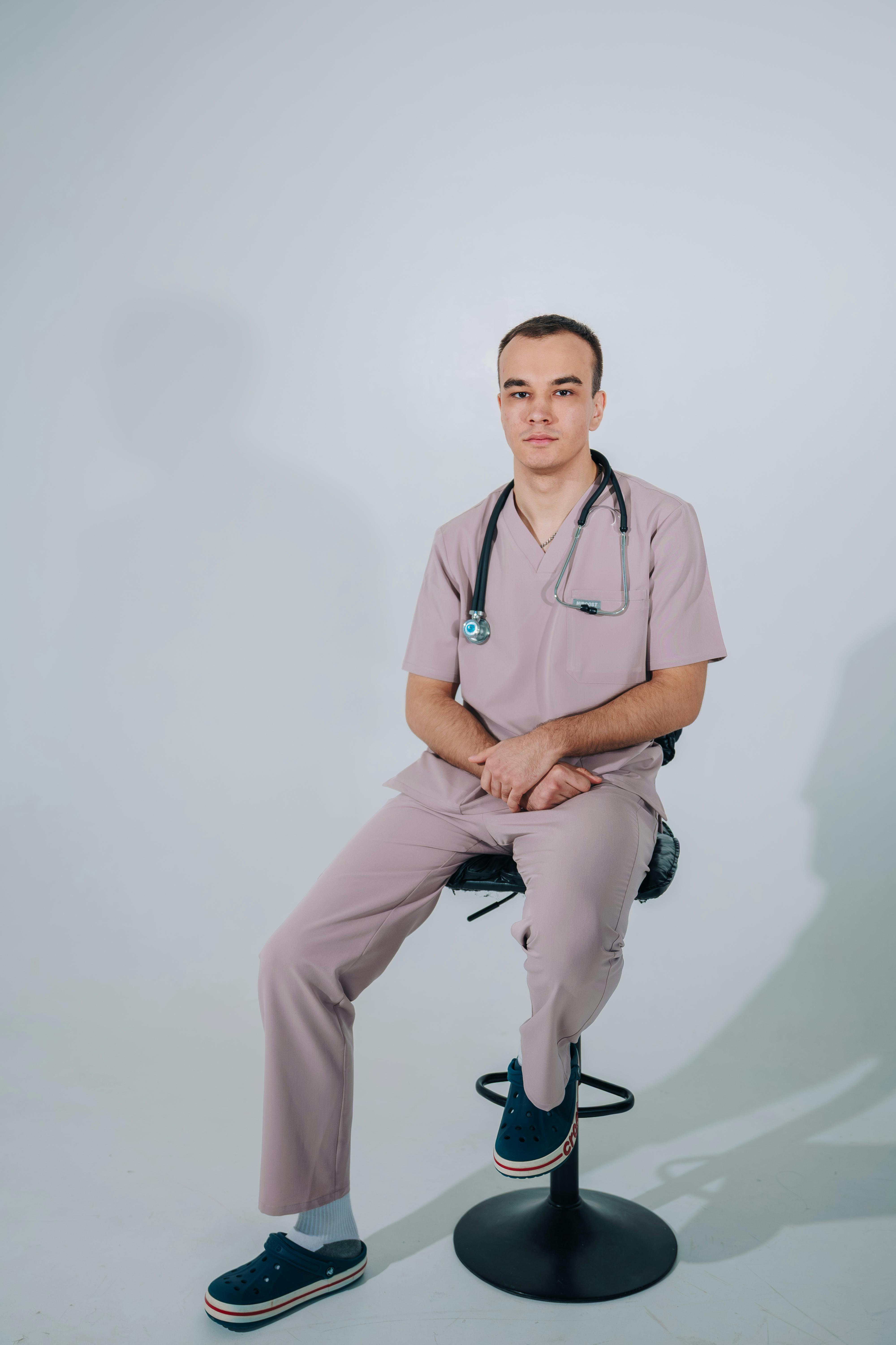 Portrait of a male nurse sitting with stethoscope in a well-lit studio.