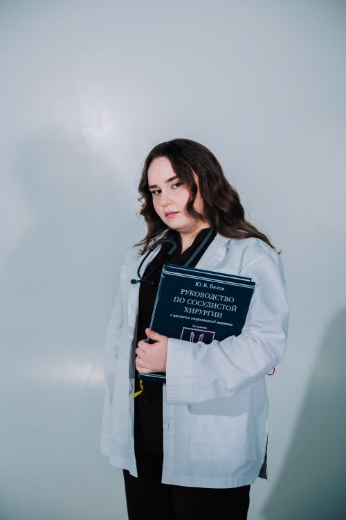 Free Young female doctor holding a vascular surgery guide, dressed in a white coat, standing confidently. Stock Photo