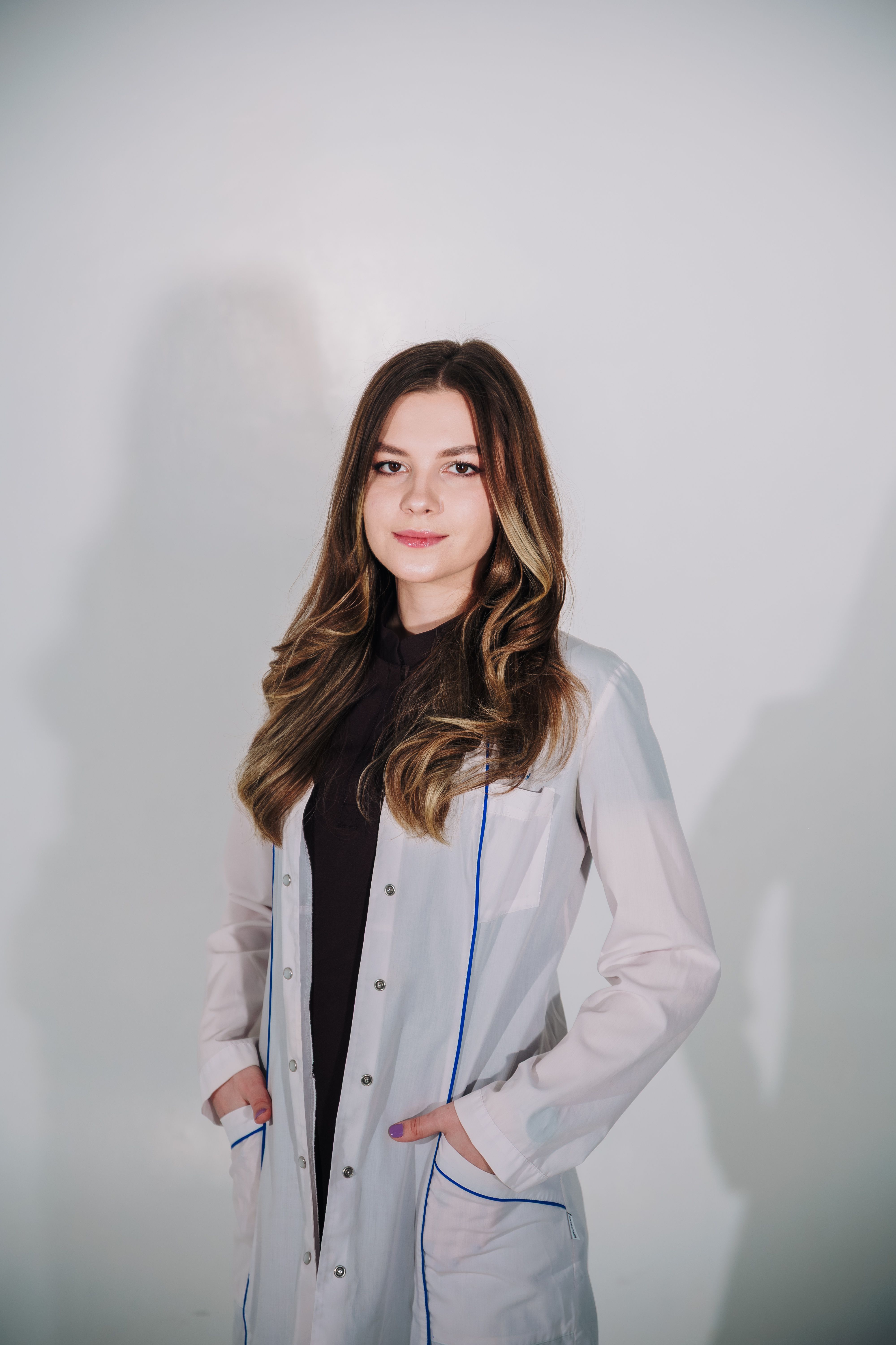 A young female scientist confidently poses in a lab coat with a neutral background.