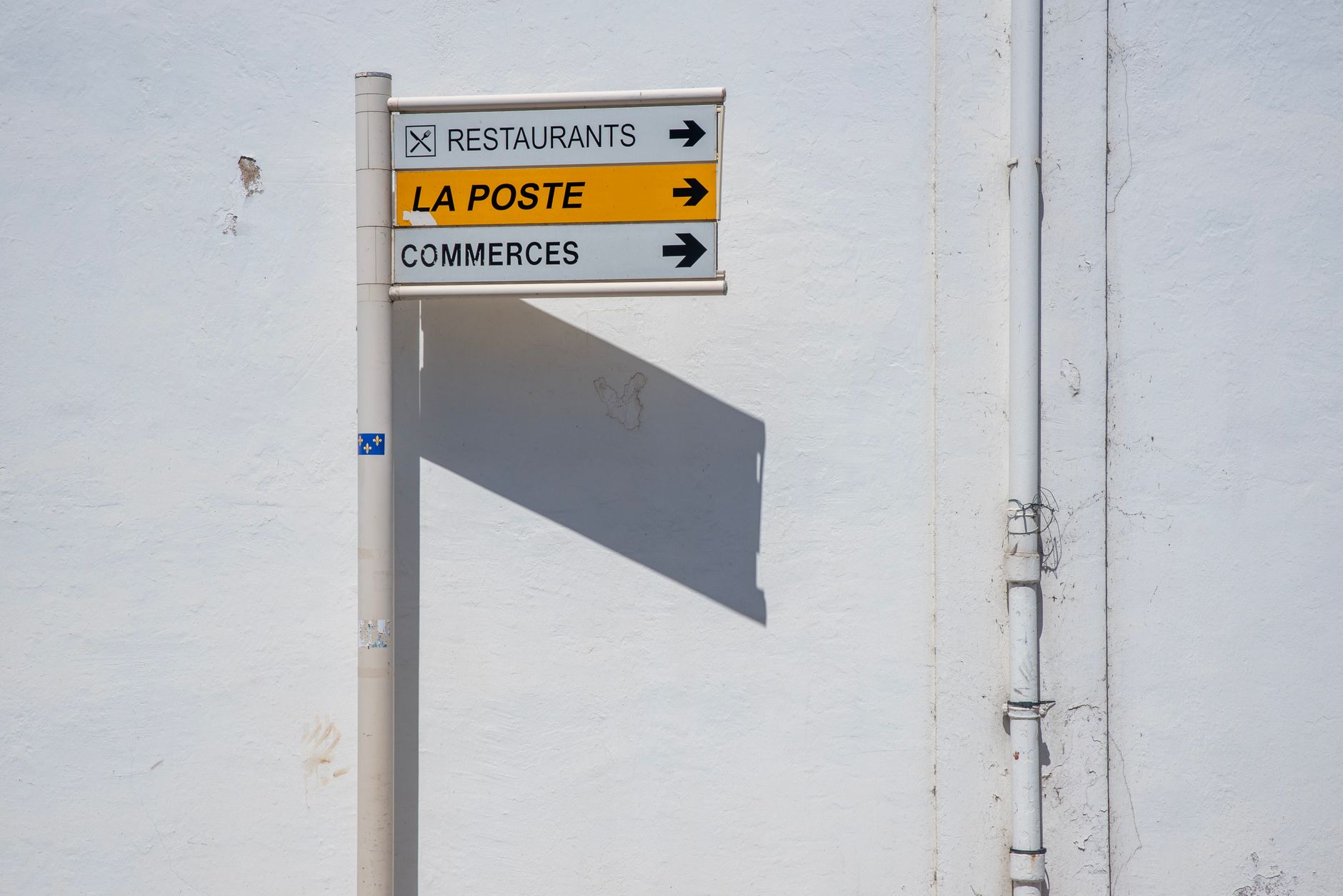 Street direction sign pointing towards La Poste, restaurants, and commerces.