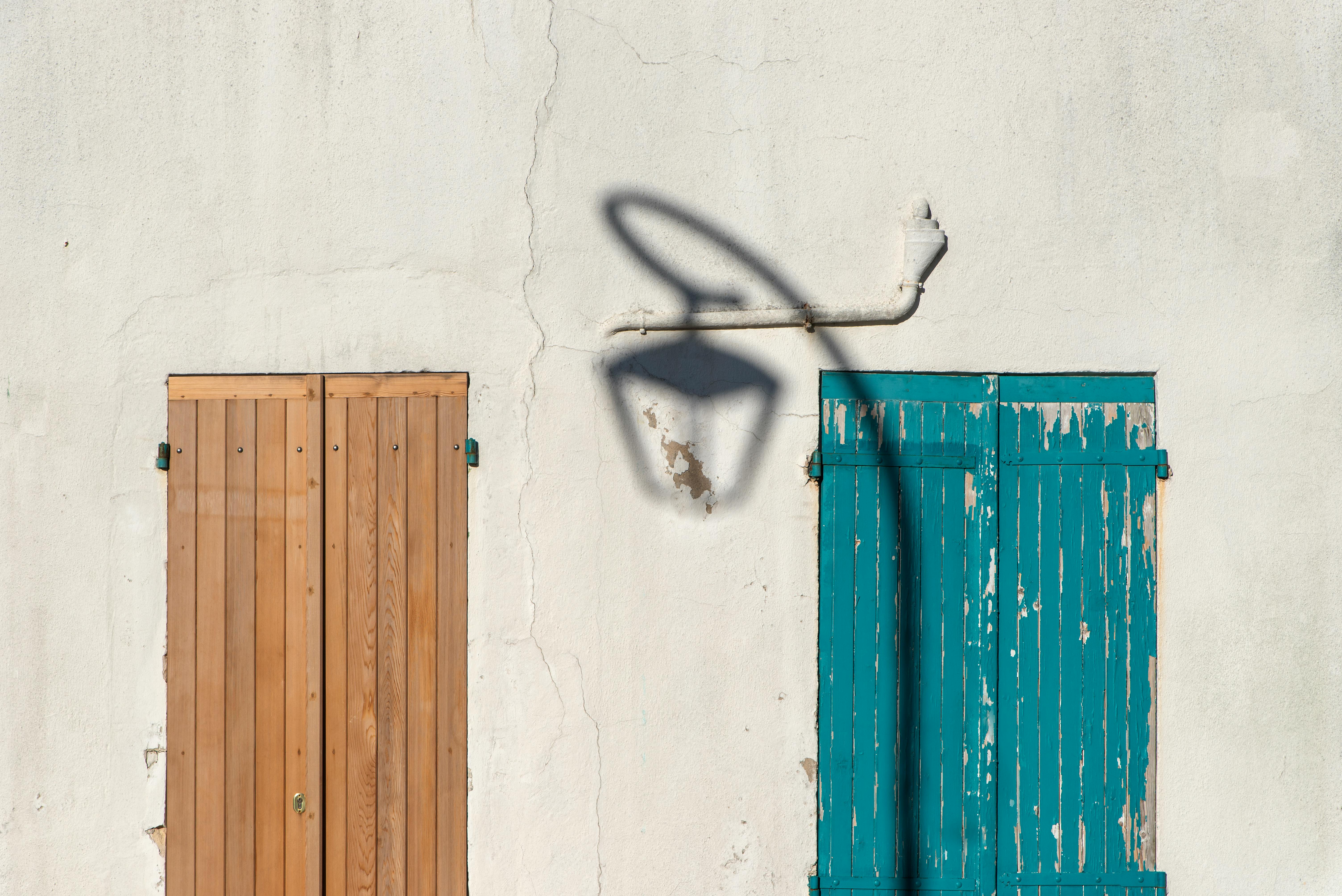 Rustic wooden and teal shutters with a vintage streetlight shadow on a textured wall.