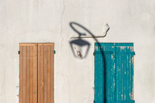 Free Rustic wooden and teal shutters with a vintage streetlight shadow on a textured wall. Stock Photo