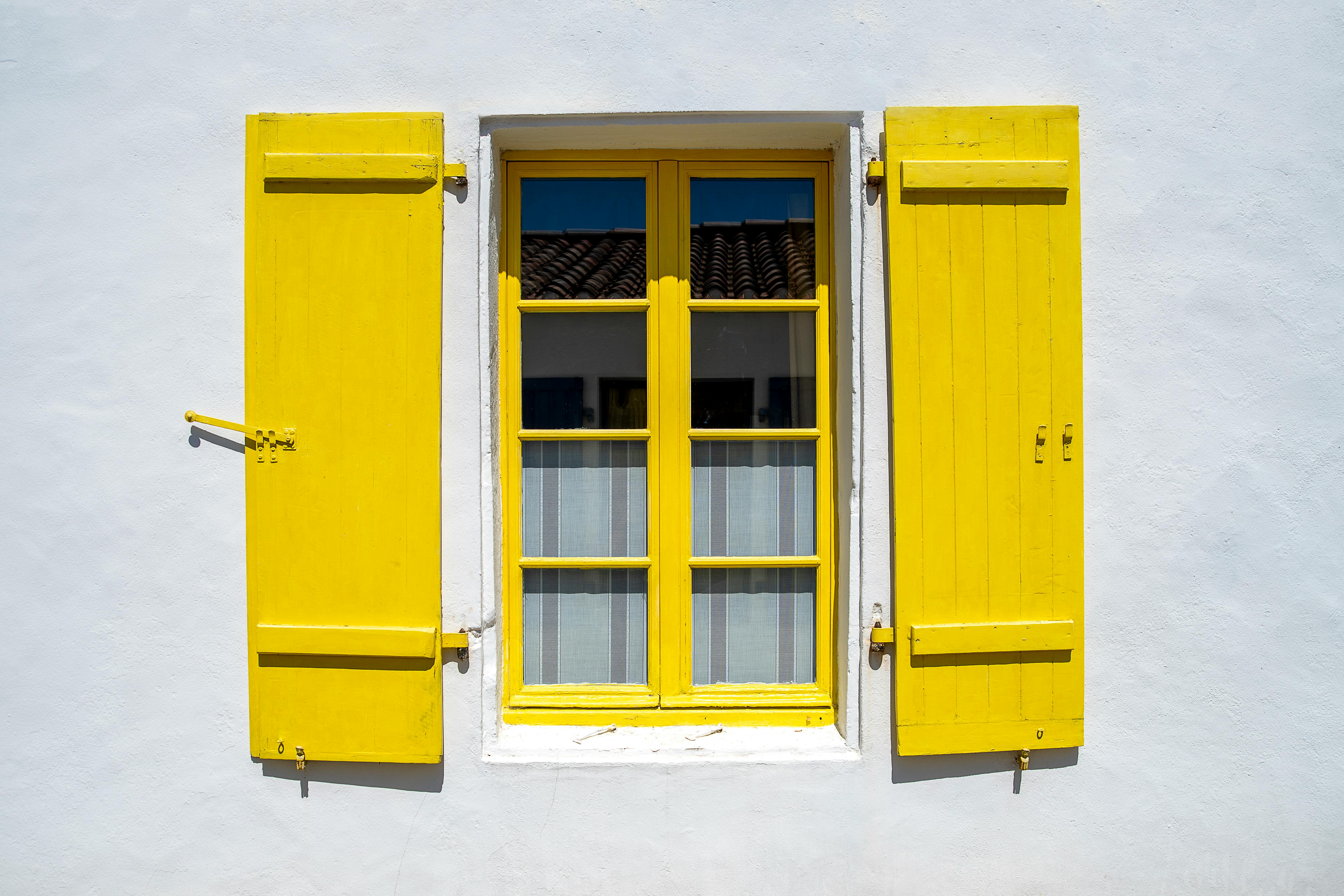 Bright yellow window shutters on a white wall add a cheerful pop to an architectural scene.