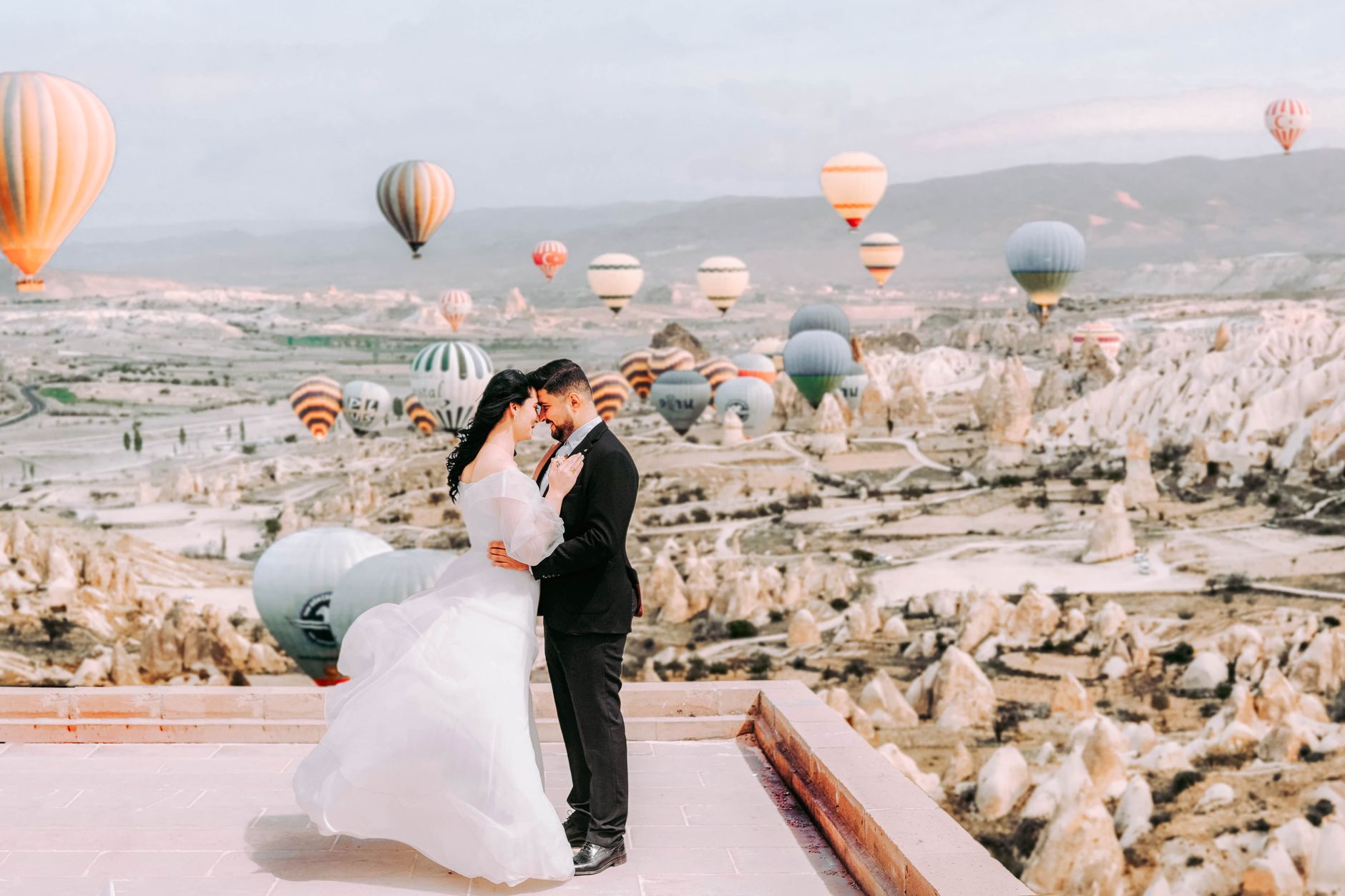 Elegant wedding couple embracing with hot air balloons in Cappadocia, Turkey, creating a dreamy romantic scene.