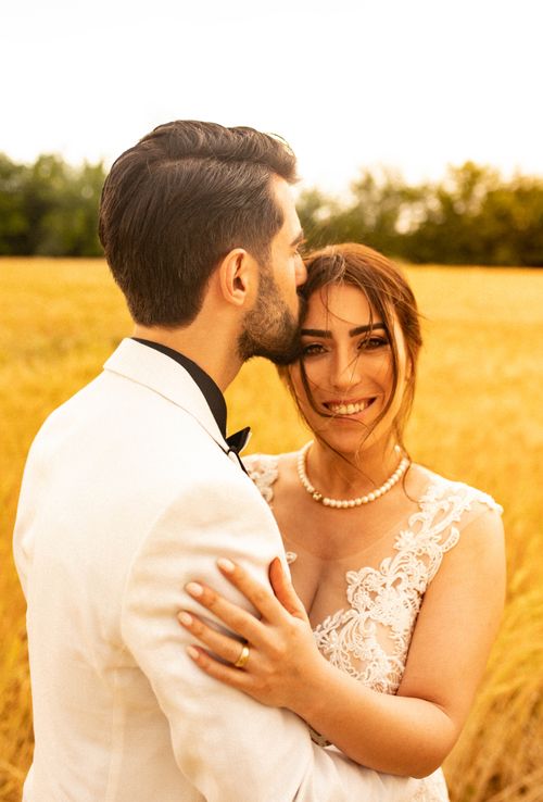 Free Bride and groom embracing in sunlit wheat field, capturing love and happiness. Stock Photo