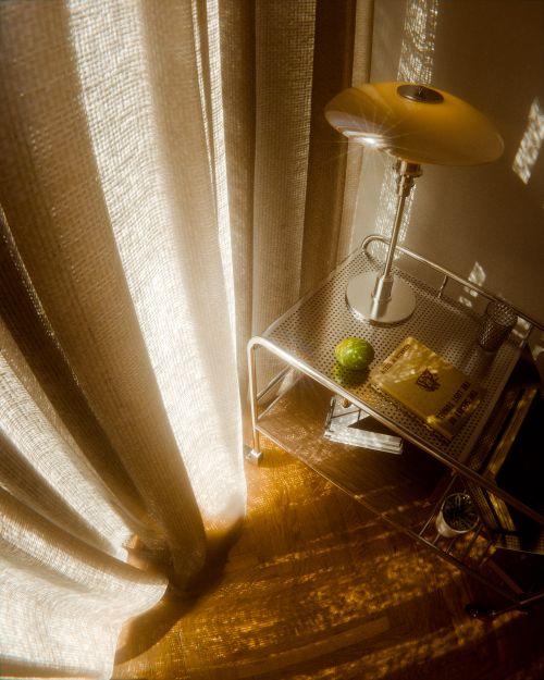 Free Warm sunlight casts shadows on a minimalist reading nook with a lamp and books. Stock Photo