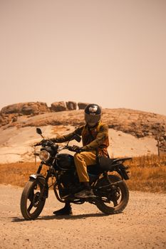 A motorcyclist rides on a desert road with rocky terrain, wearing safety gear and helmet.