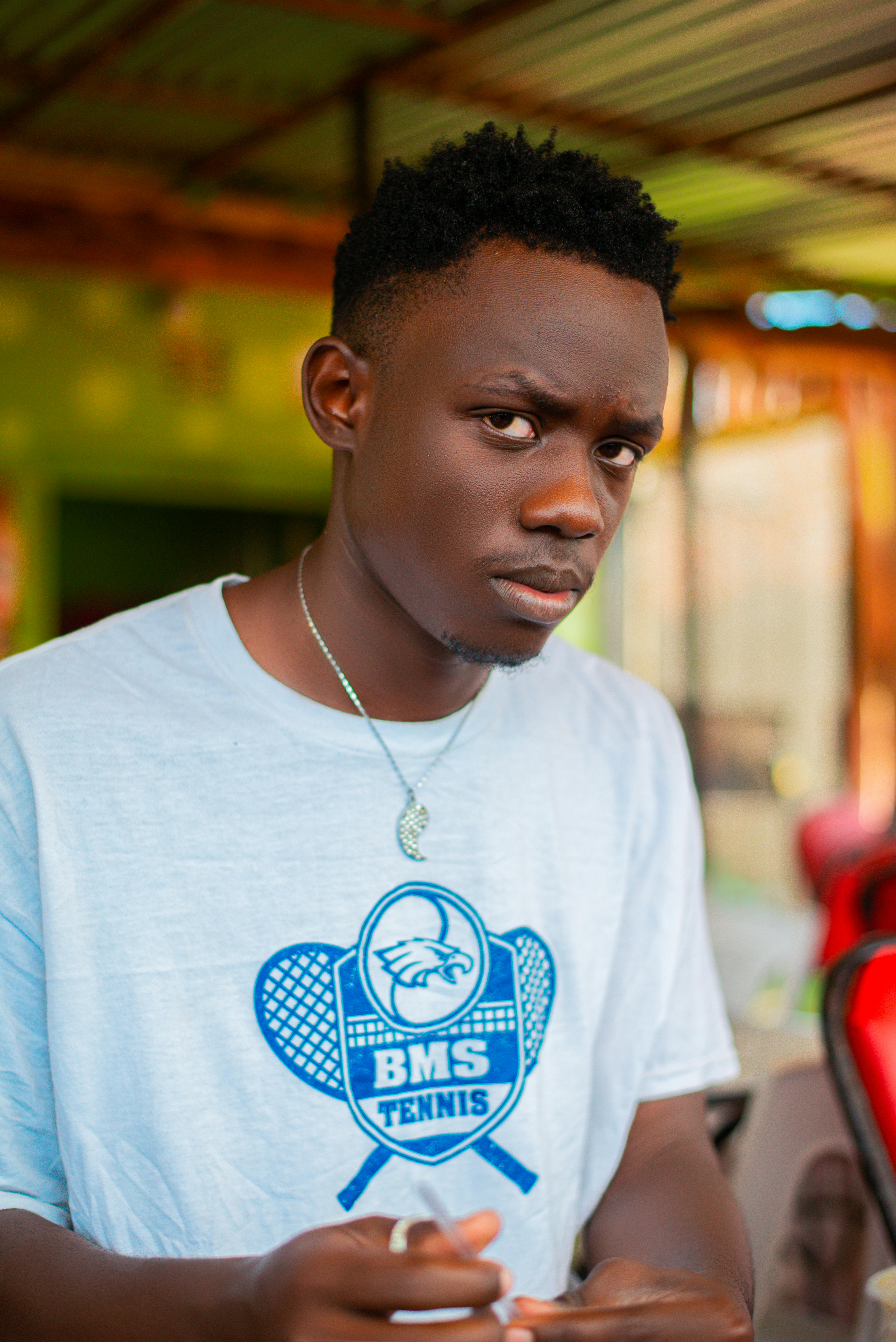 Young man indoors wearing a white tennis shirt with a thoughtful expression.