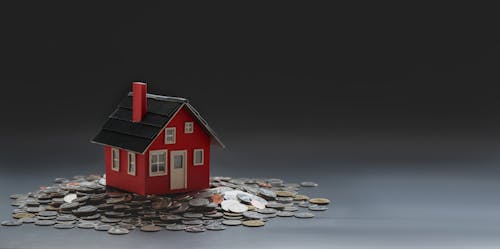 Red toy house placed on table with pile of coins