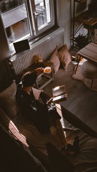 A person enjoys reading in a cozy sunlit nook with tea and cushions.