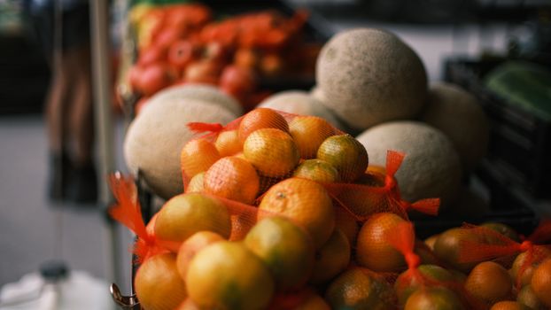 Close-up of fresh oranges and melons on display at an outdoor market, showcasing vibrant colors and textures.