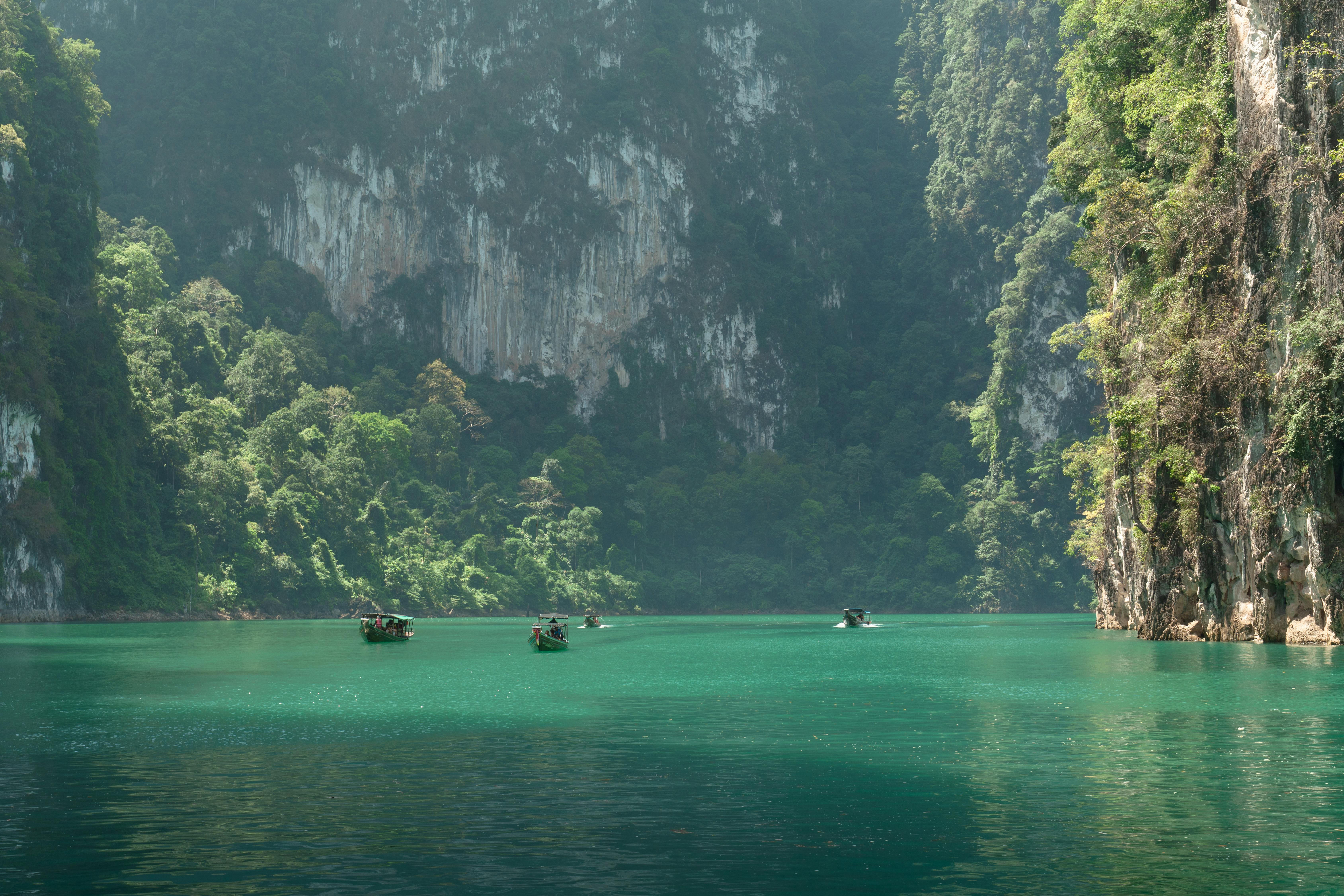 Traditional boats navigate through a serene turquoise lagoon surrounded by lush cliffs.
