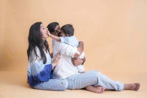 Free A family of three sharing a joyful moment in a cozy indoor environment with a warm backdrop. Stock Photo