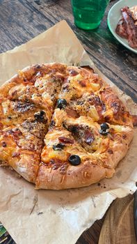 Freshly baked homemade pizza topped with olives and cheese on a wooden table.