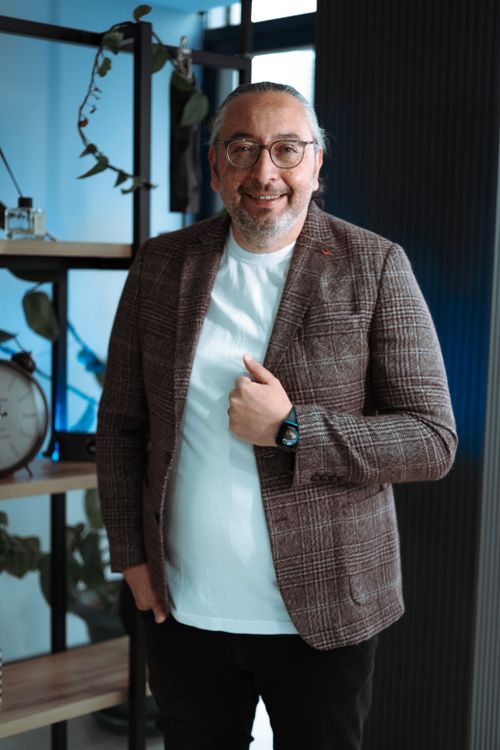 Free Middle-aged man smiling in an office environment, surrounded by shelves and plants. Stock Photo