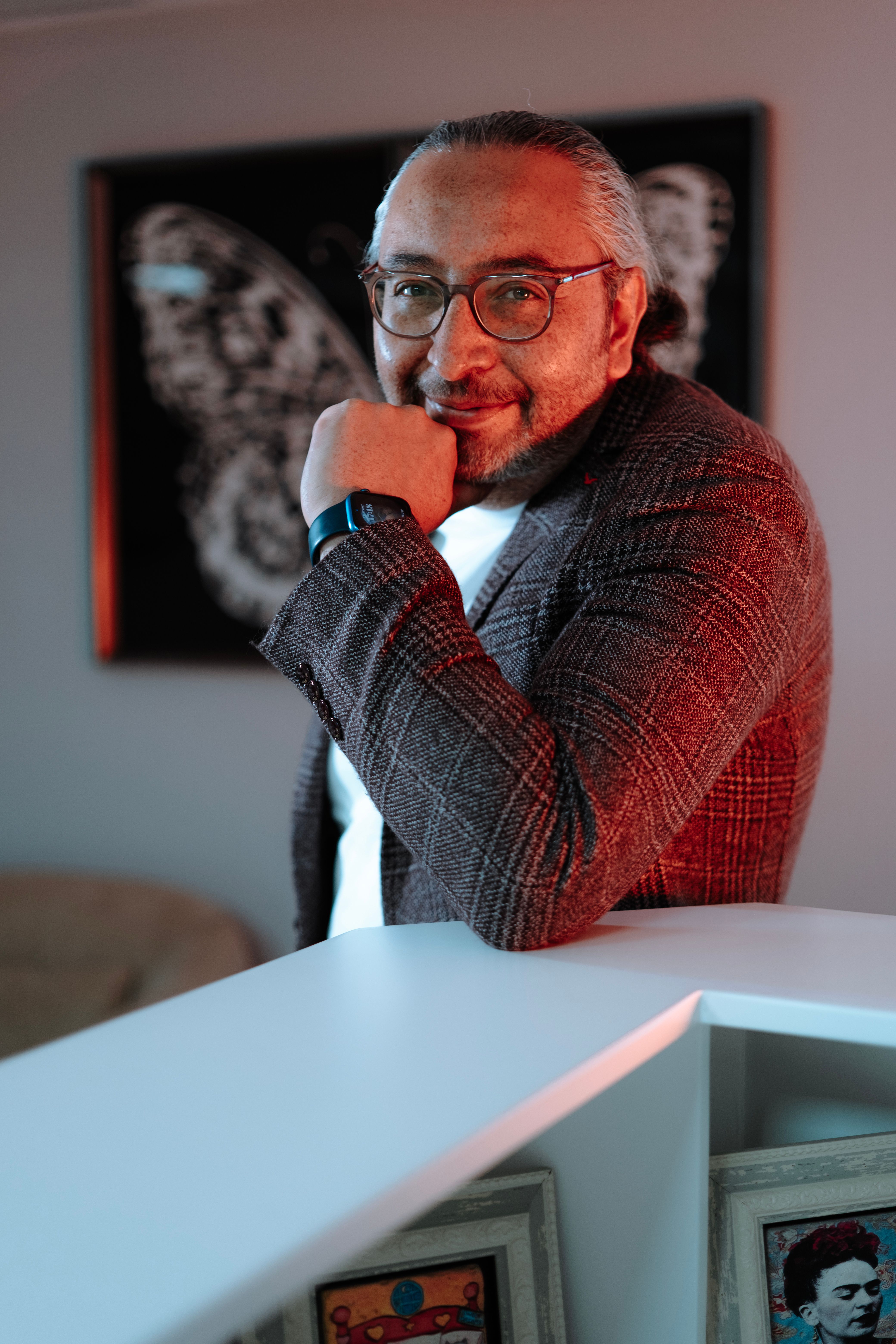 Confident businessman in glasses and suit posing with a smile in a modern, artistic office setting.