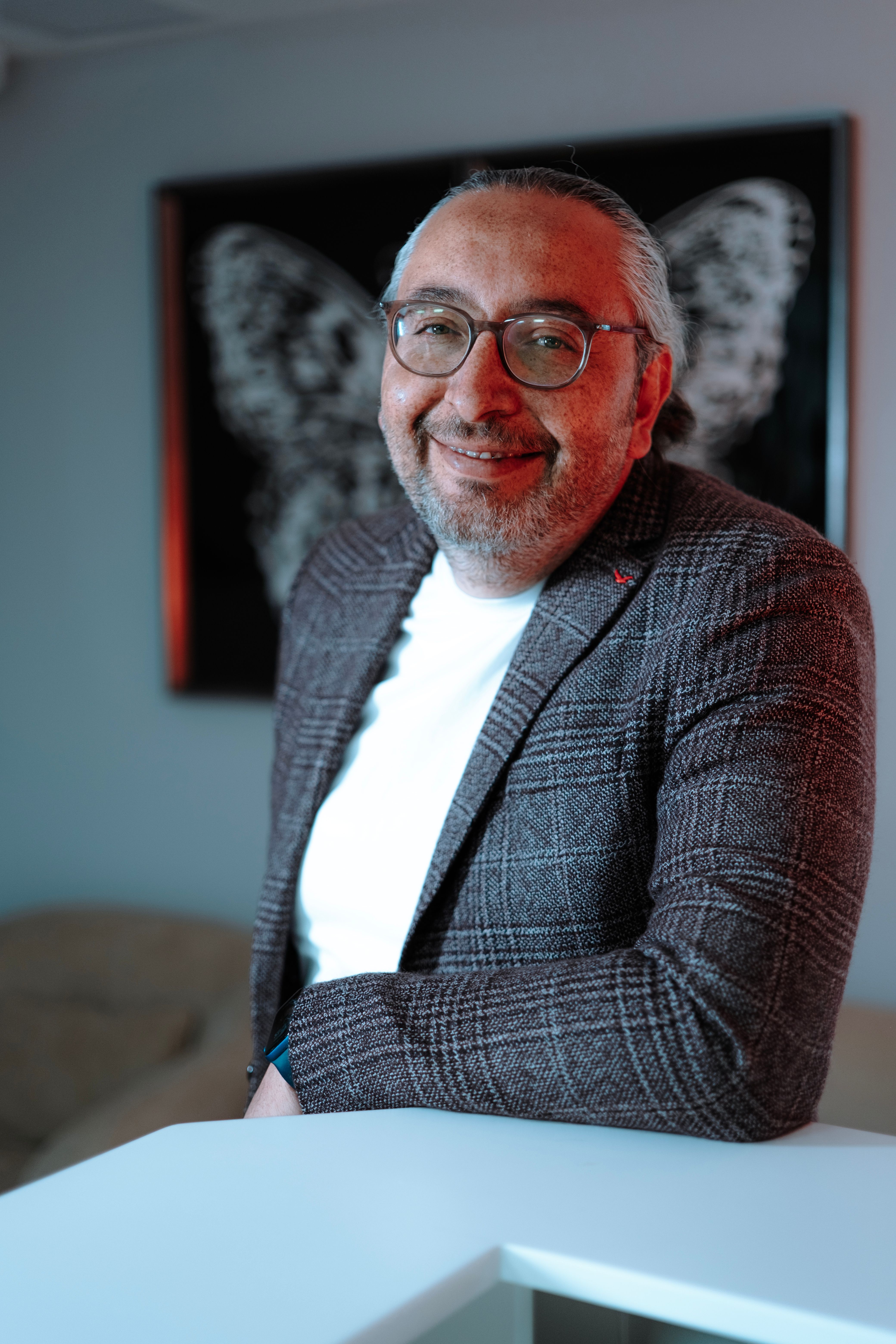 Smiling man in glasses and suit indoors against butterfly artwork background.