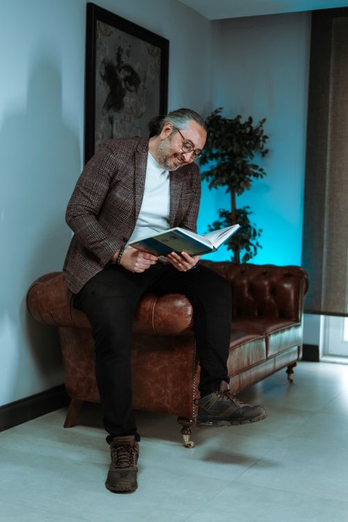 Free Middle-aged man sitting on leather couch reading a book in a stylish living room setting Stock Photo
