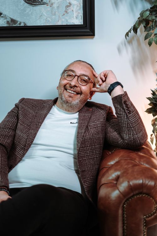 Free Smiling man in casual attire relaxing on a leather couch with a framed painting behind. Stock Photo