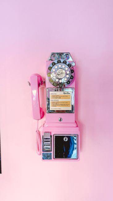 A nostalgic pink rotary dial payphone decorates a soft pink wall, blending vintage charm with modern aesthetics.