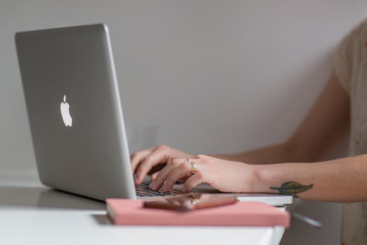 Close-up of a woman typing on a laptop at a modern, minimalist desk with a phone nearby.