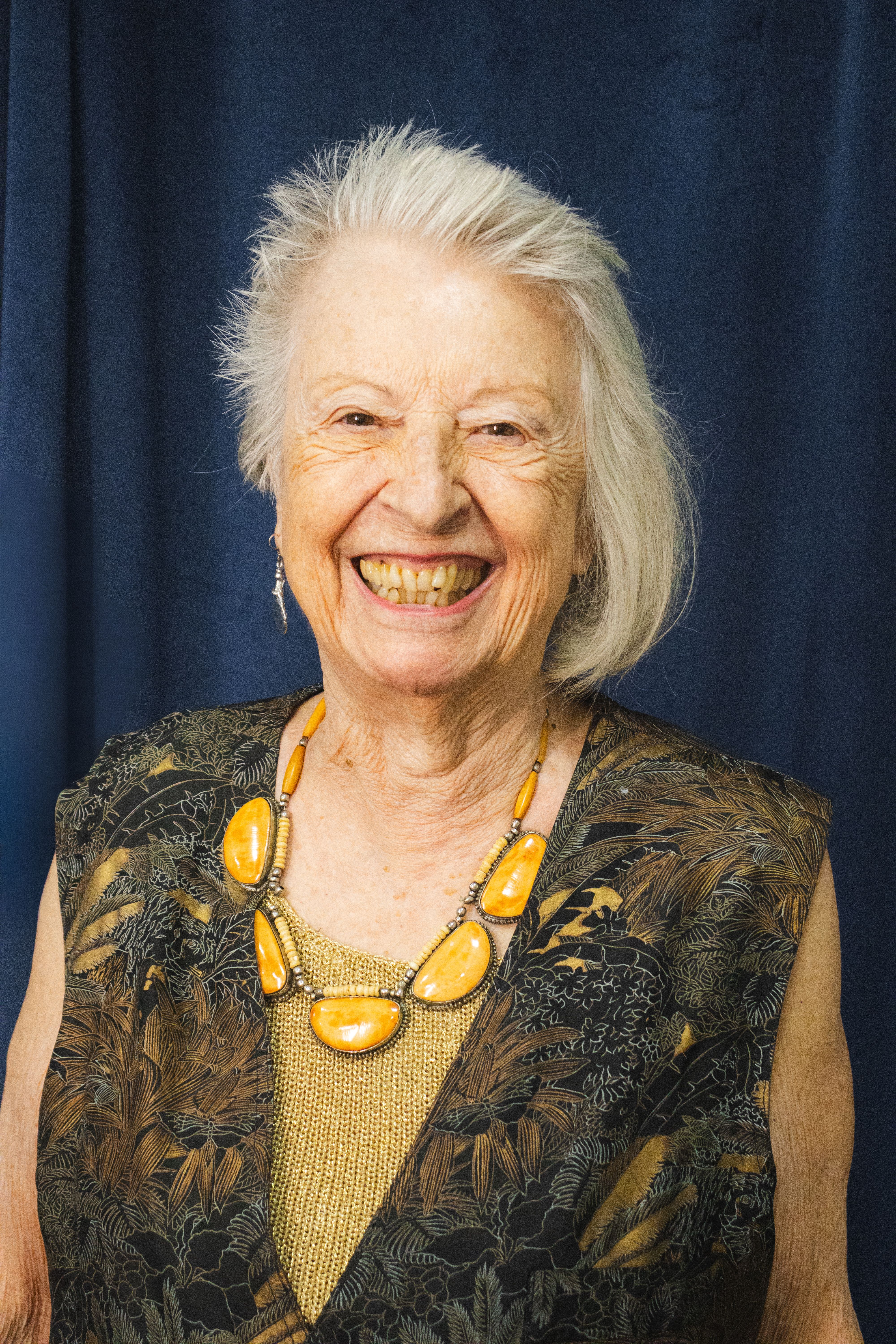 Elderly woman with a joyful smile, wearing an ornate necklace, photographed indoors.