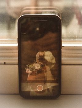 Creative reflection of floral bouquet captured through smartphone camera on window sill.