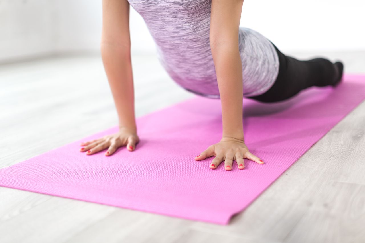 A woman performs a yoga stretch indoors on a pink mat