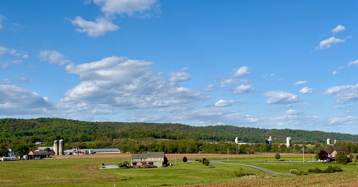 A picturesque view of Pennsylvania farmland under a clear blue sky with rolling hills.