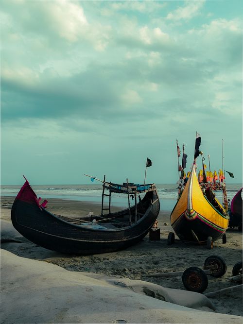 Free Colorful fishing boats rest on the serene Cox's Bazar beach in Bangladesh under a cloudy sky. Stock Photo
