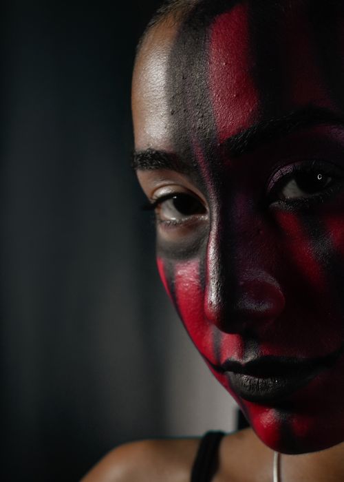 Free Portrait featuring intricate red and black artistic face paint on a woman's face. Stock Photo