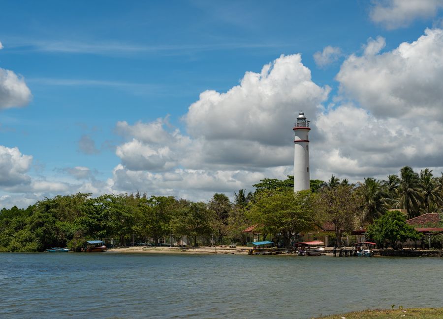 Beautiful coastal scene featuring the iconic Batticaloa Lighthouse amidst lush greenery under a vibrant blue sky.