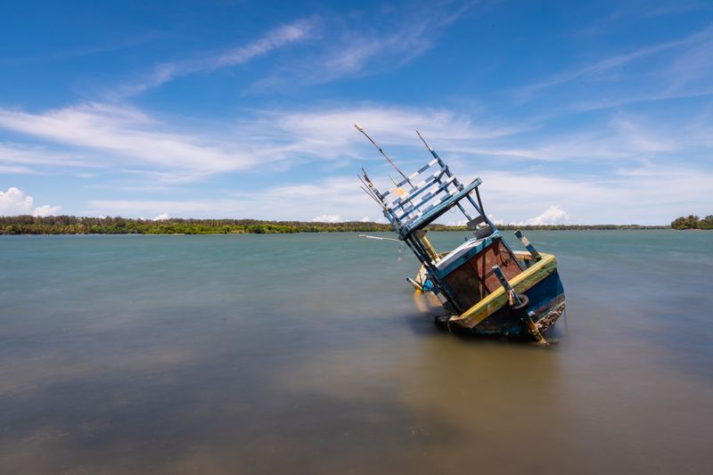 A tilted fishing boat rests in the tranquil waters of Batticaloa Lagoon, Sri Lanka, under a clear blue sky.