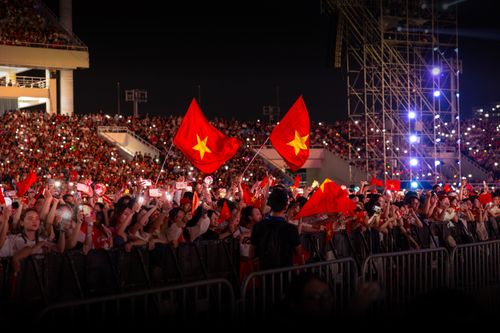 Free A nighttime concert with a large, energetic crowd waving flags under bright lights. Stock Photo