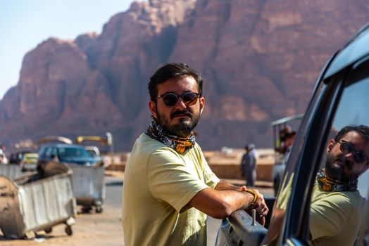 A man stands confidently by a car with a stunning rocky mountain background in Ürdün.