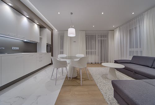 Minimalist modern design of kitchen with white cabinets and gray sofa in contemporary illumination