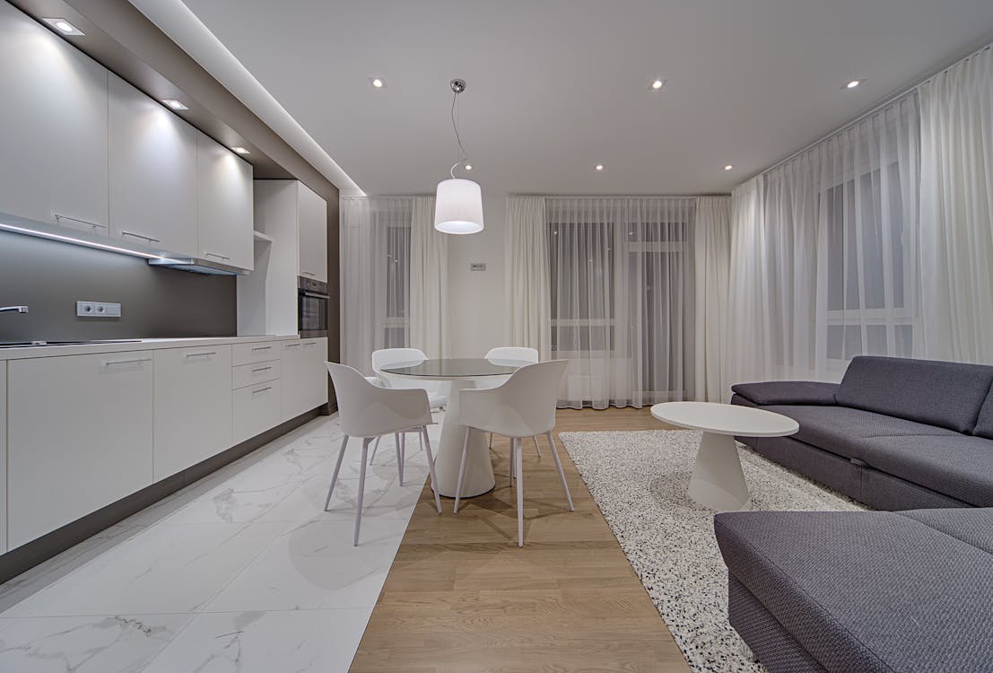 Minimalist modern design of kitchen with white cabinets and gray sofa in contemporary illumination