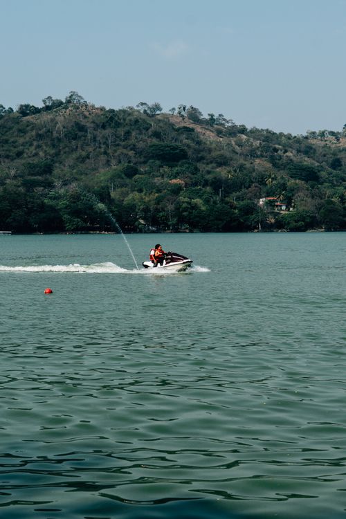 Free Couple enjoying a thrilling jet ski ride on a serene lake surrounded by lush hills. Stock Photo