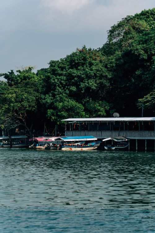 Free Calm waters and vibrant boat scene captured along a lush riverside. Stock Photo