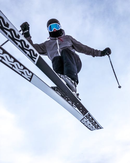 From below of agile person in helmet and winter outerwear skiing and flying in jump under blue sky