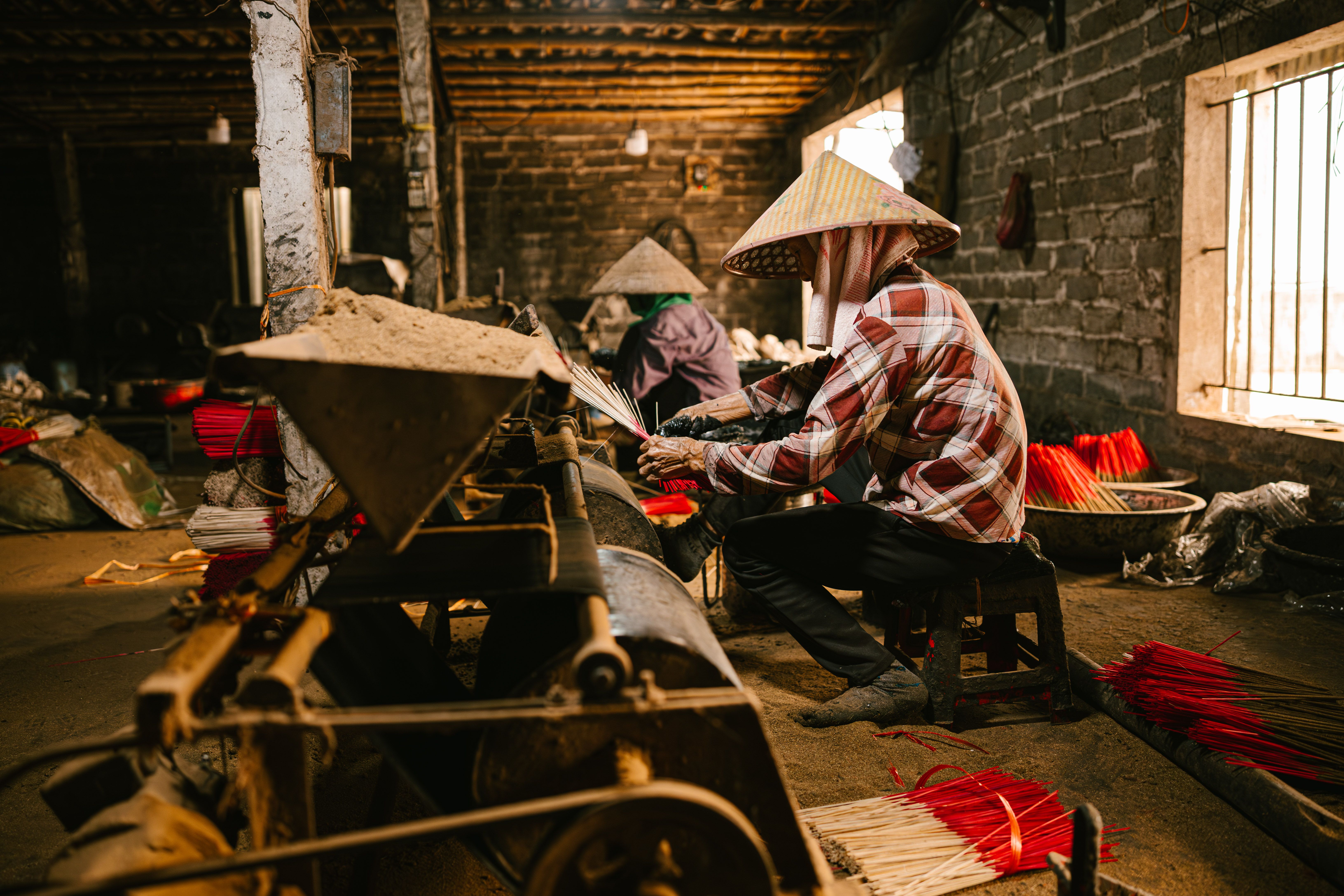 Artisans crafting traditional incense sticks in a rural workshop with natural lighting and rustic surroundings.