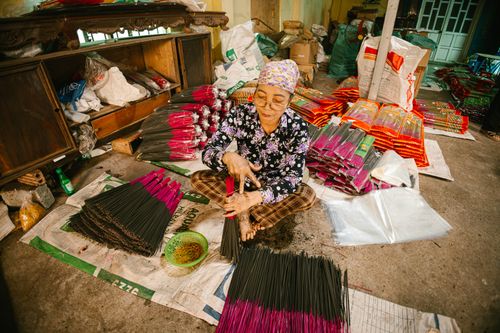 Free An elderly woman skillfully crafting incense sticks in a traditional workshop setting, surrounded by materials. Stock Photo