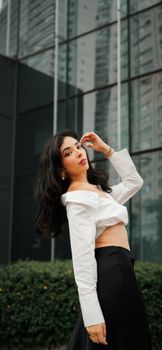 Stylish woman in white blouse and black skirt posing against a modern cityscape