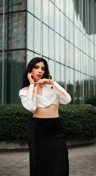 Stylish woman in modern attire posing against a glass building backdrop.
