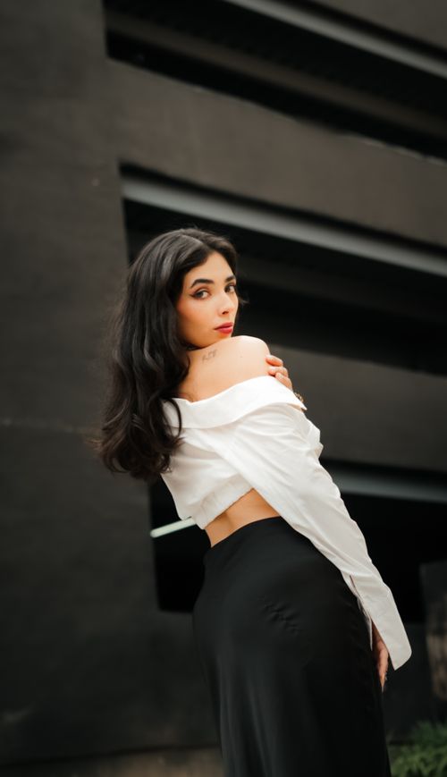 Free Chic woman in white blouse and black skirt poses elegantly in an urban setting. Stock Photo
