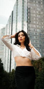 Stylish woman posing confidently against a backdrop of modern urban skyscrapers.
