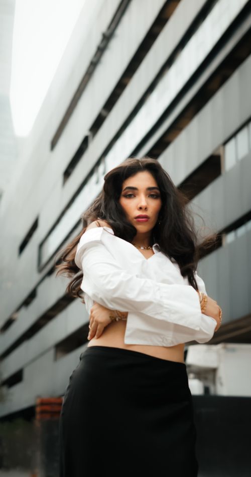 Free A fashionably dressed woman poses confidently in front of a modern urban building. Stock Photo
