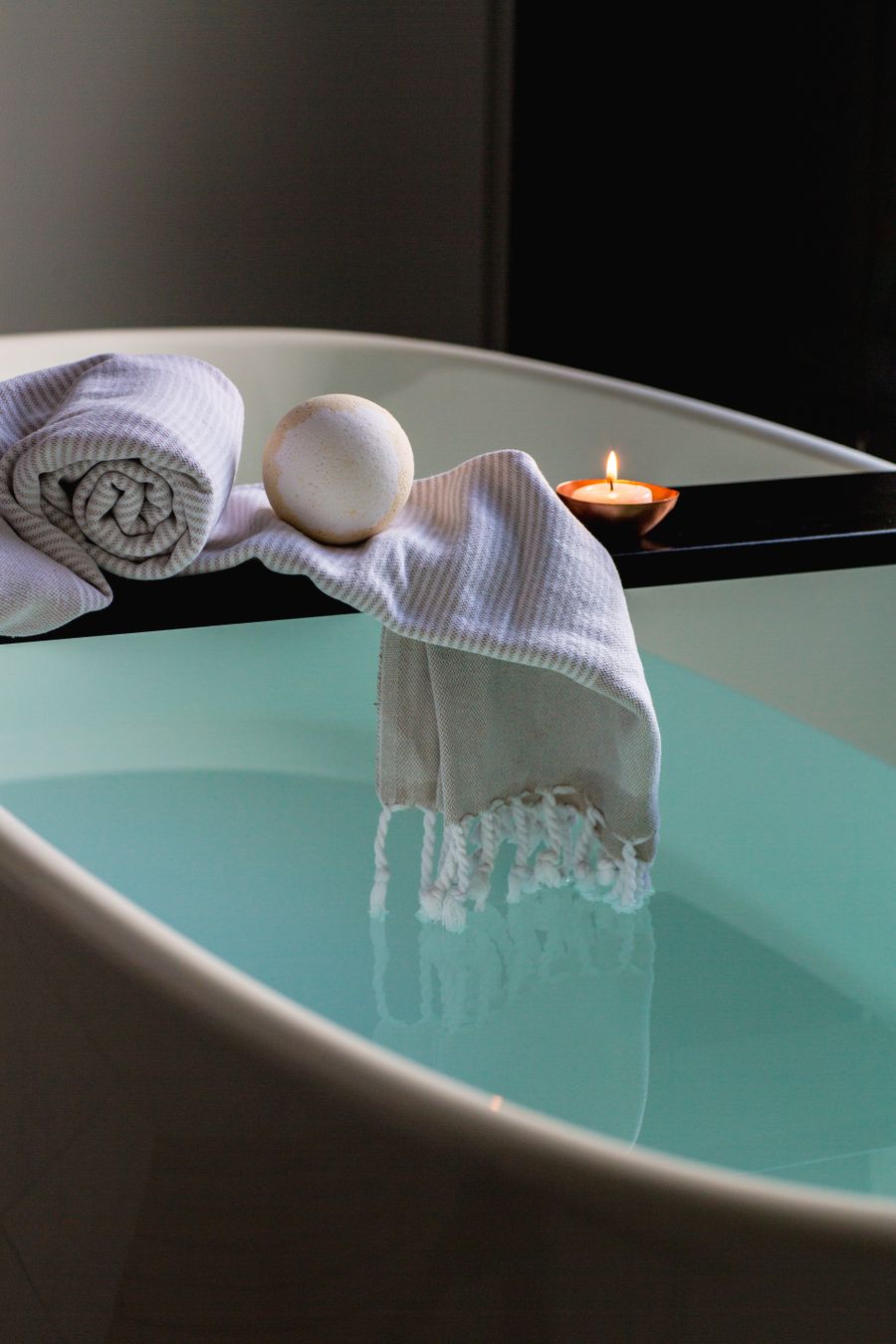Bathtub with a lit candle and towels in a spa-like bathroom